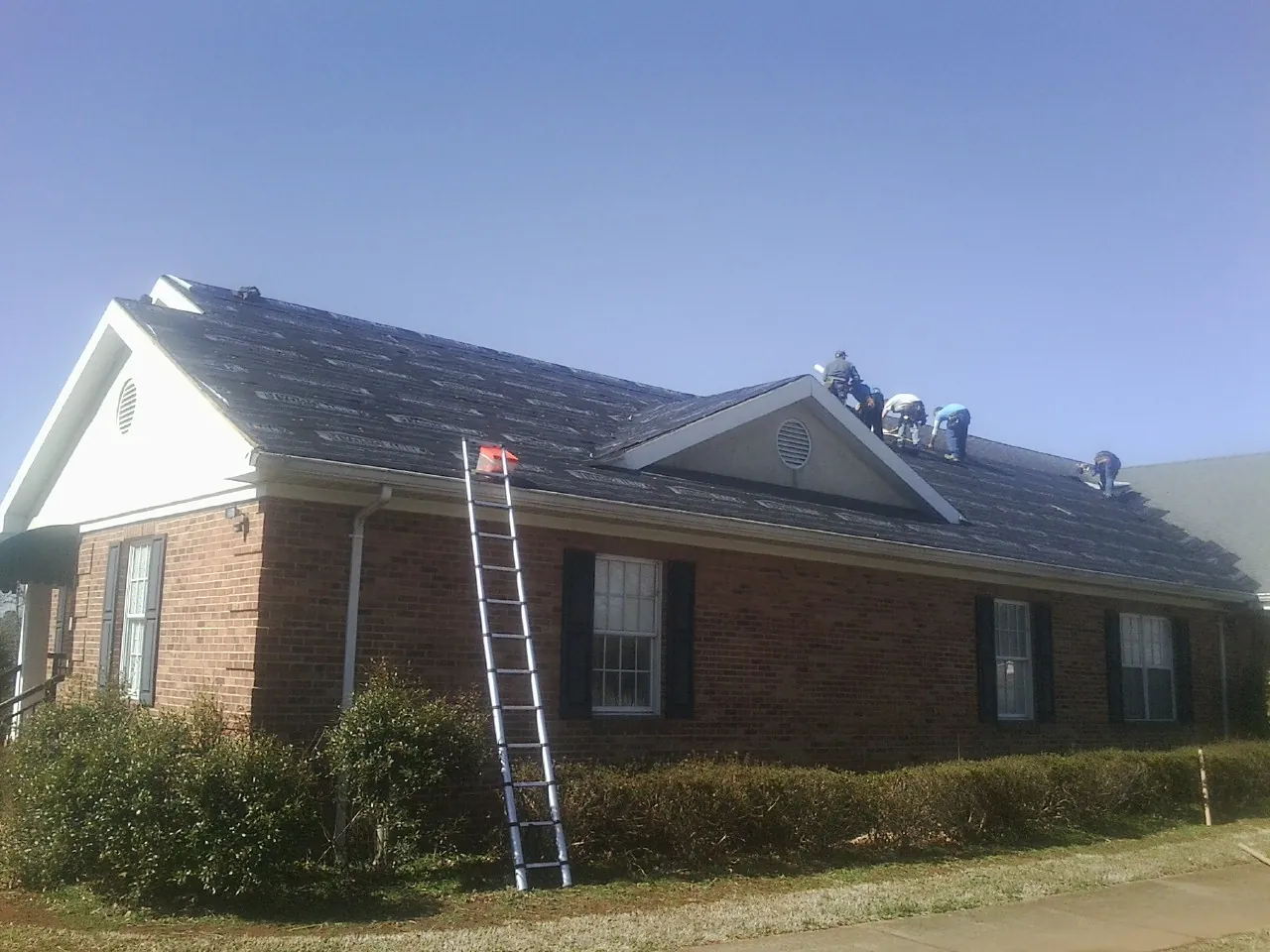 Crew tearing shingles off a brick ranch roof with a ladder set — Metal Roof Repair work by our crew in Yorktown