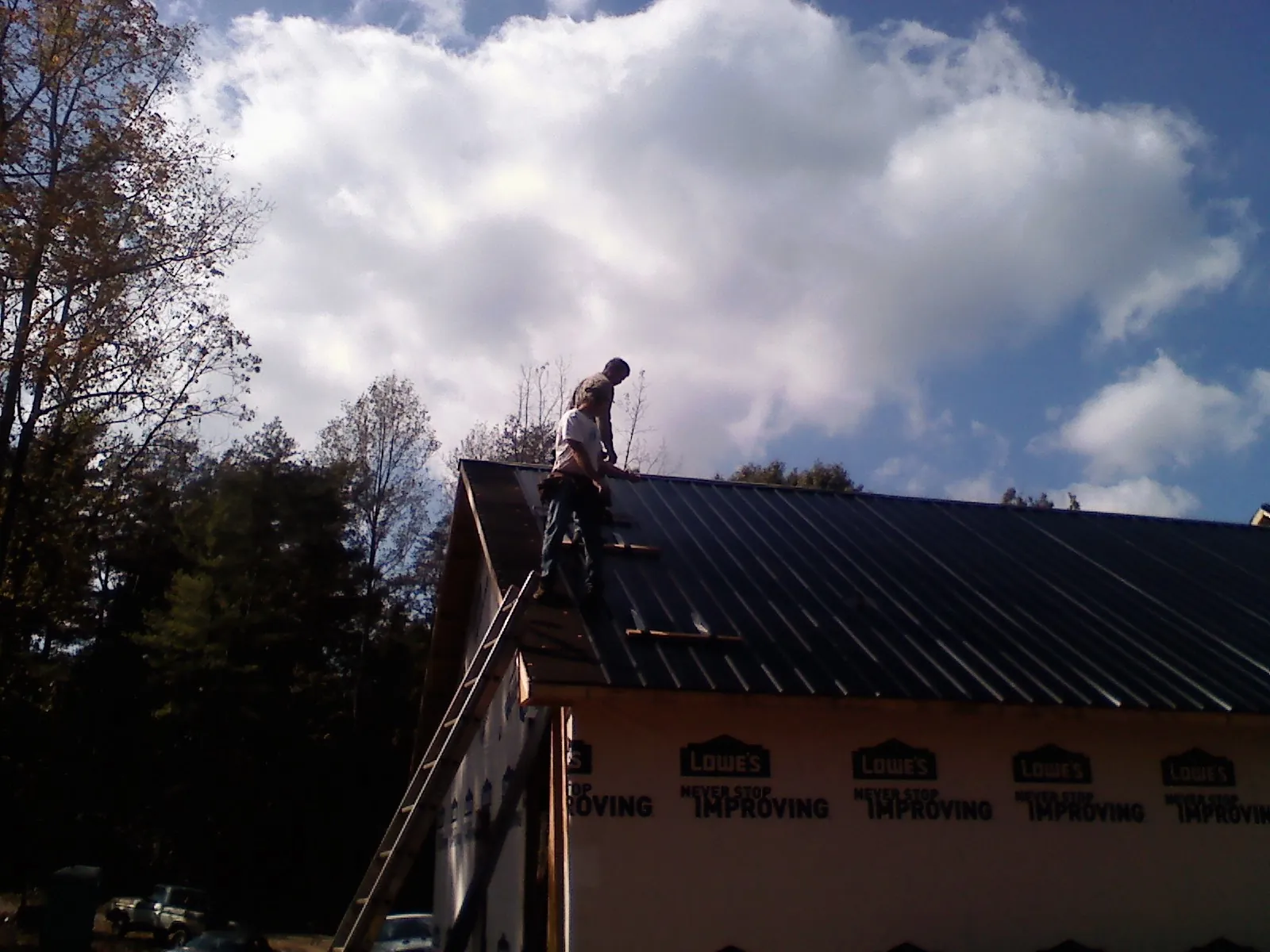 Roofer fastening dark metal panels high against a cloudy sky, from a Roof Inspection job in Yorktown