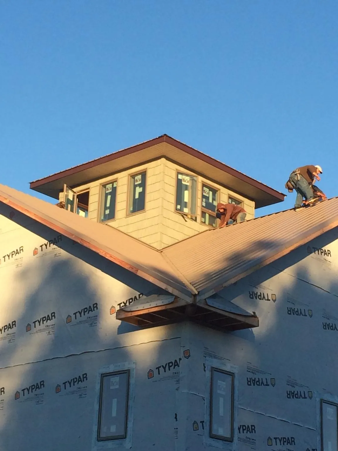 Roofers working around a rooftop cupola on a new metal roof at sunset in Yorktown